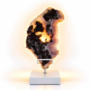 Roze Amethist Eclipse lamp op witte standaard met warme verlichting en contrasterende donkere mineraalstructuren