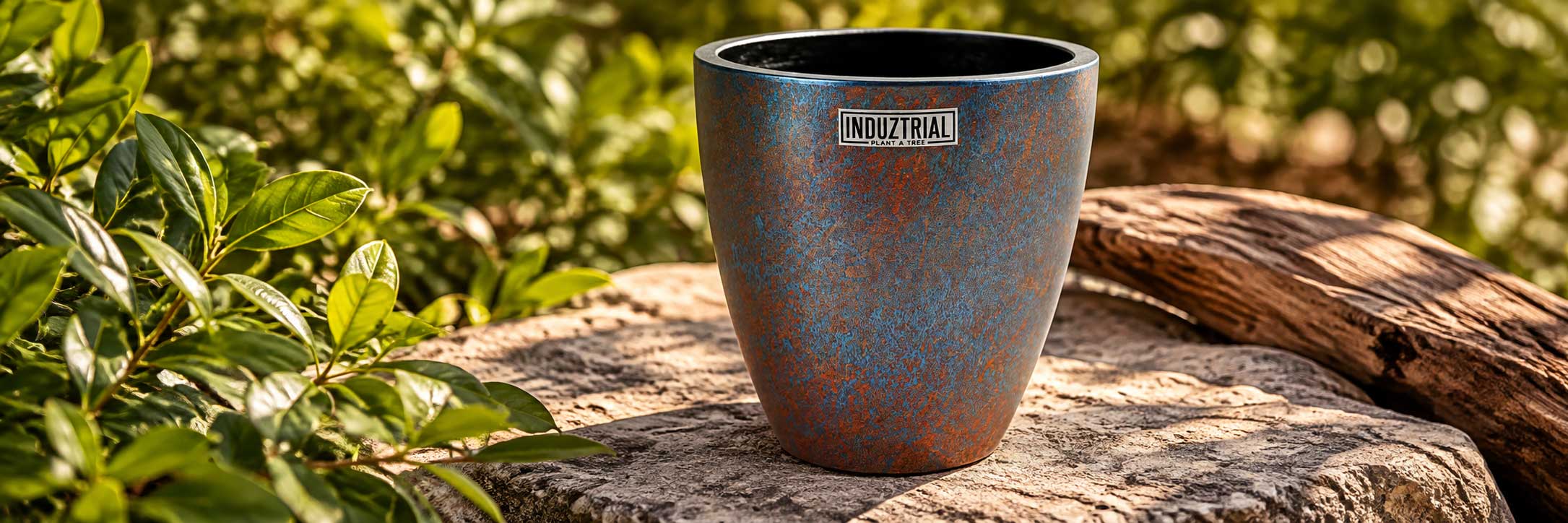 Handgeschilderde vaas in metallic blauw en roesttinten in een natuurlijke buitenomgeving