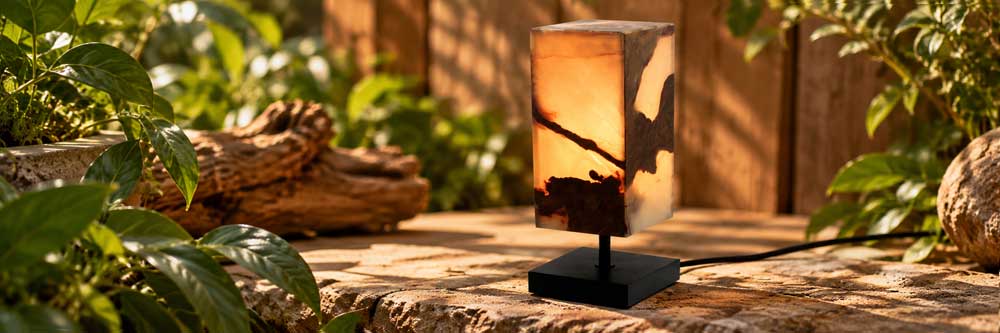 White en Dark Onyx edelsteen lamp met warme amberkleurige gloed op zwarte standaard in natuurlijke setting